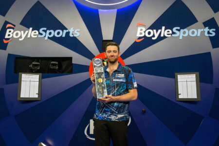 Luke Humphries holds the 2023 World Grand Prix trophy on stage
