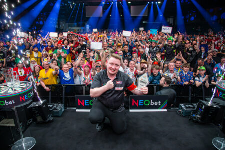 Martin Schindler poses with the International Darts Open trophy in Riesa, with the crowd cheering behind him.